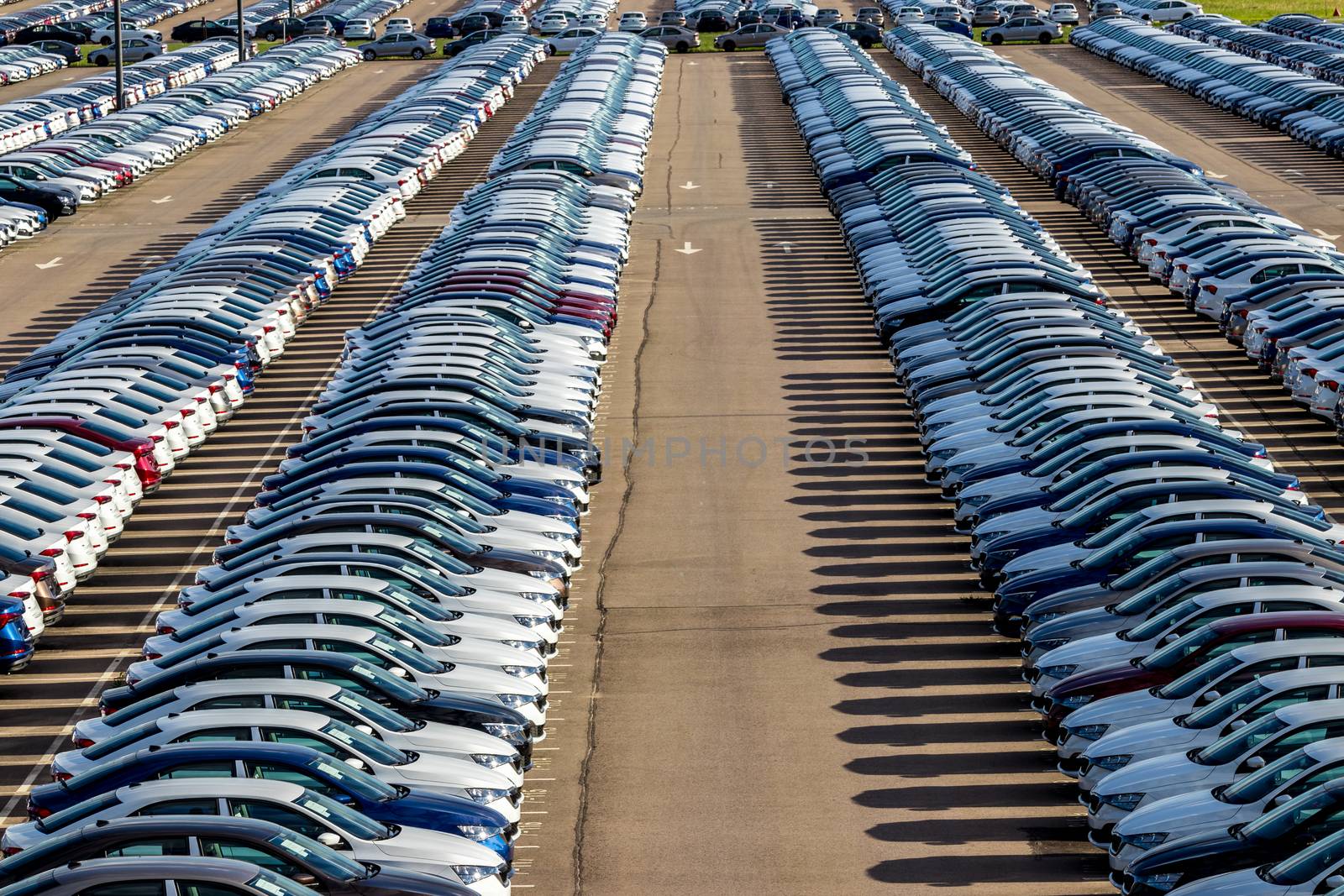 Rows of a new cars parked in a distribution center on a car factory on a sunny day. Top view to the parking in the open air.