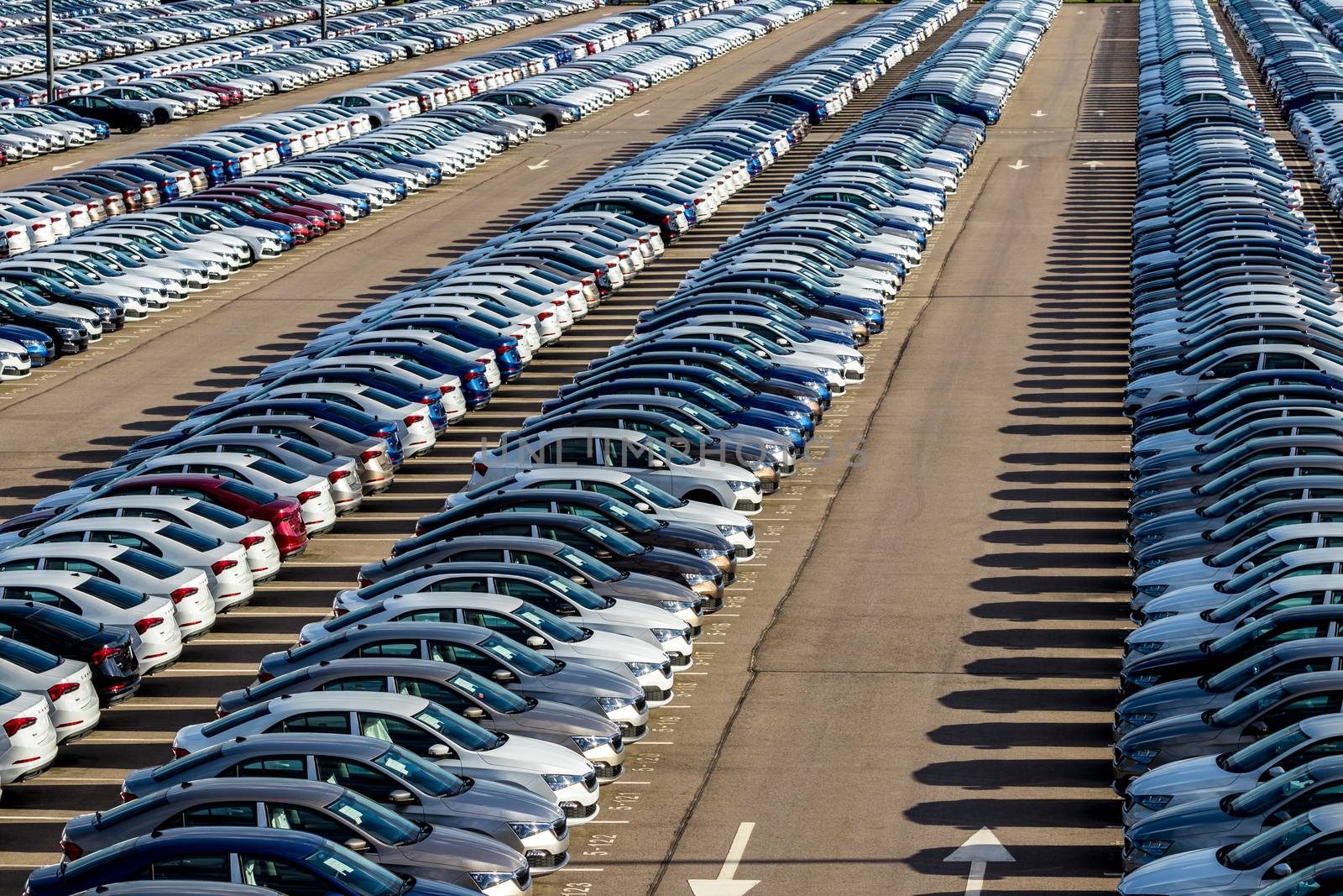 Rows of a new cars parked in a distribution center on a car factory on a sunny day. Top view to the parking in the open air.