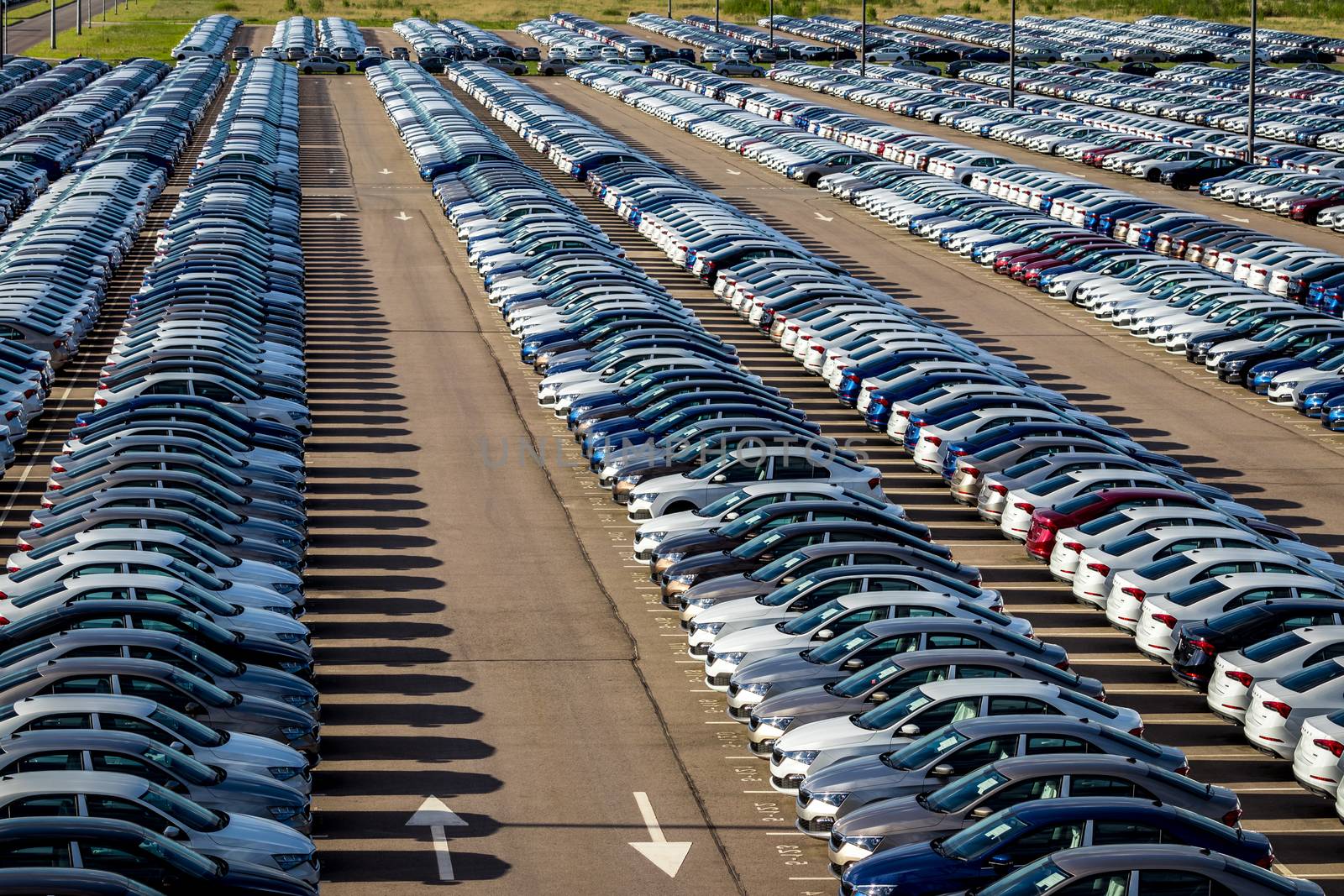 Rows of a new cars parked in a distribution center on a car factory on a sunny day. Parking in the open air.