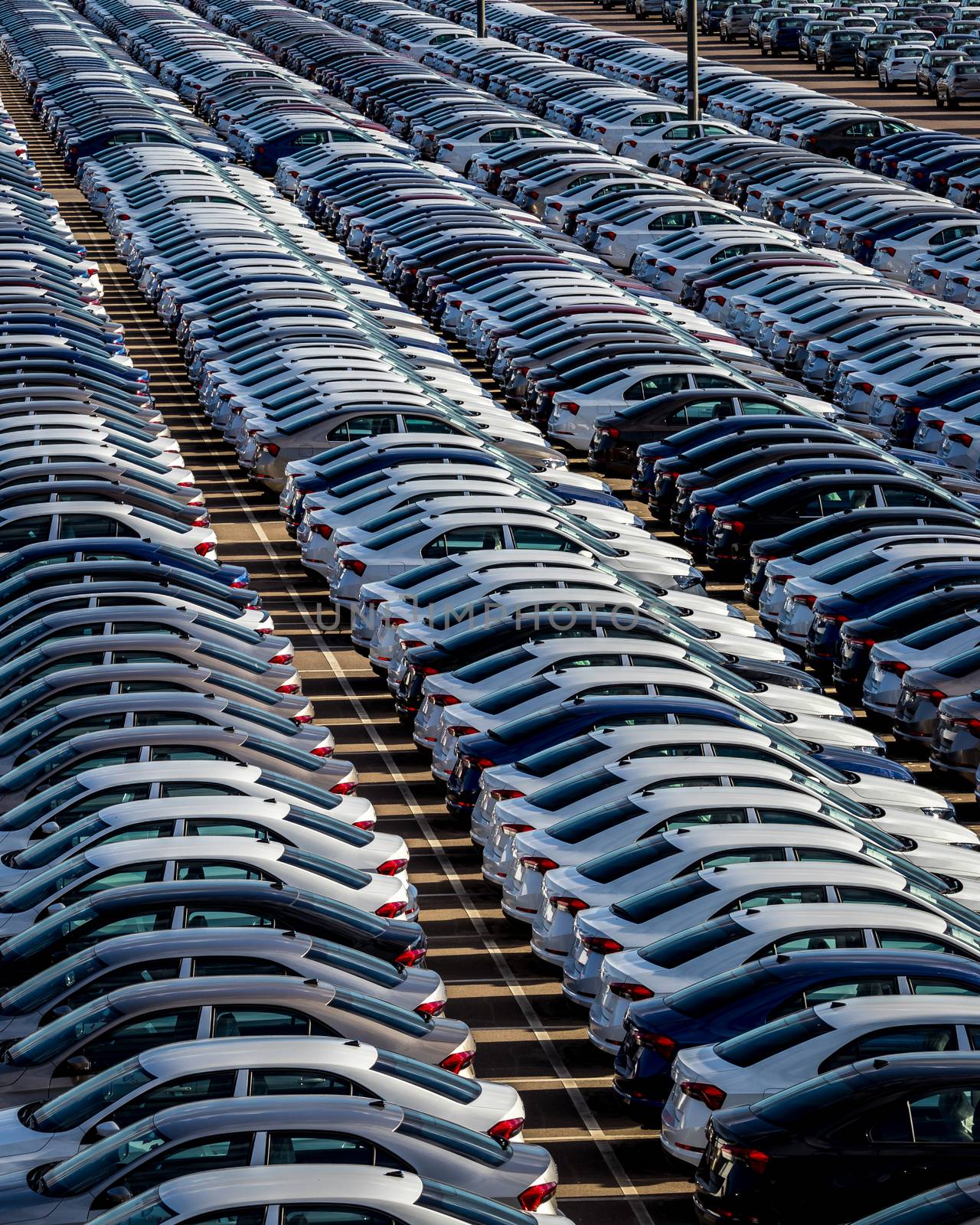 Rows of a new cars parked in a distribution center on a car factory on a sunny day. Top view to the parking in the open air.