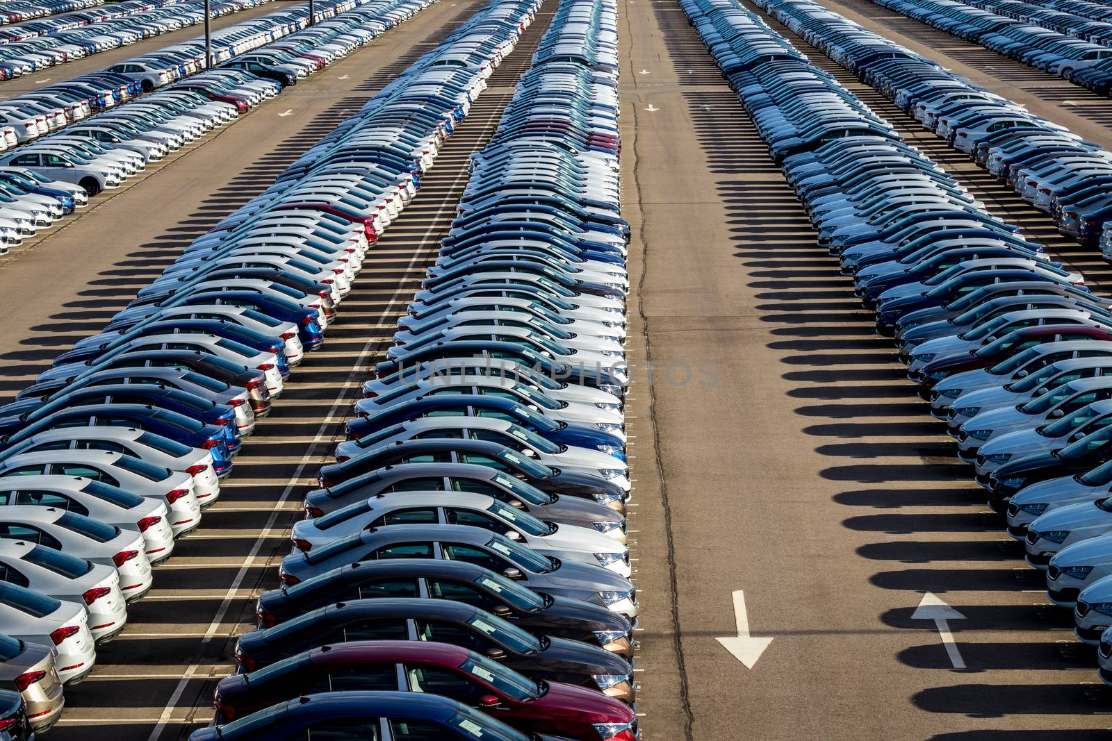 Rows of a new cars parked in a distribution center on a car factory on a sunny day. Top view to the parking in the open air.