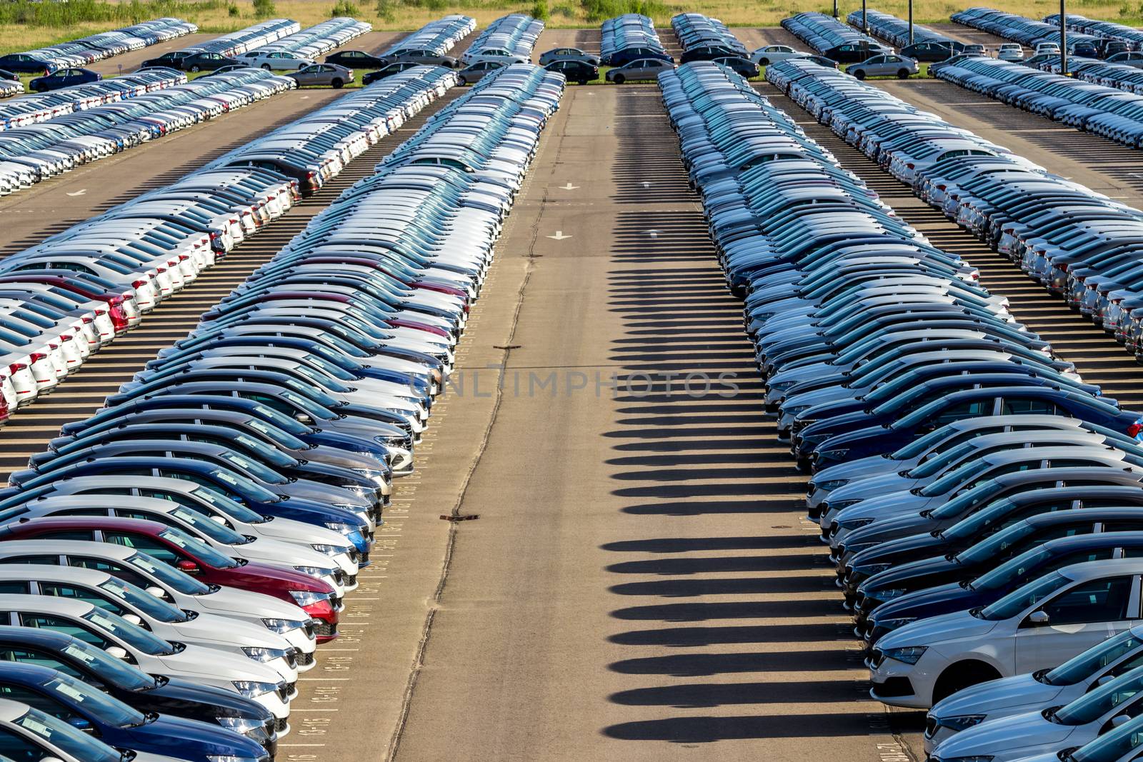 Rows of a new cars parked in a distribution center on a car factory on a sunny day. Parking in the open air.