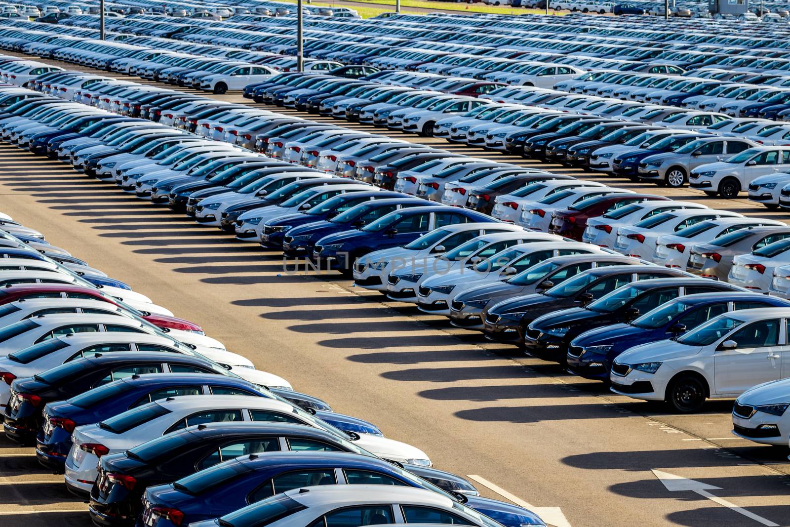 Rows of a new cars parked in a distribution center on a car factory on a sunny day. Top view to the parking in the open air.