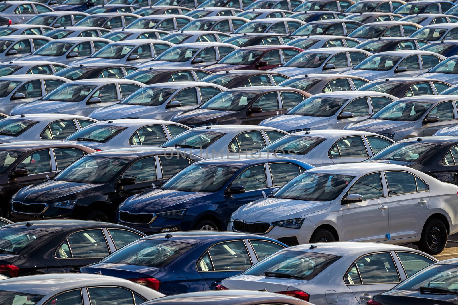 Rows of a new cars parked in a distribution center on a car factory on a sunny day. Top view to the parking in the open air.