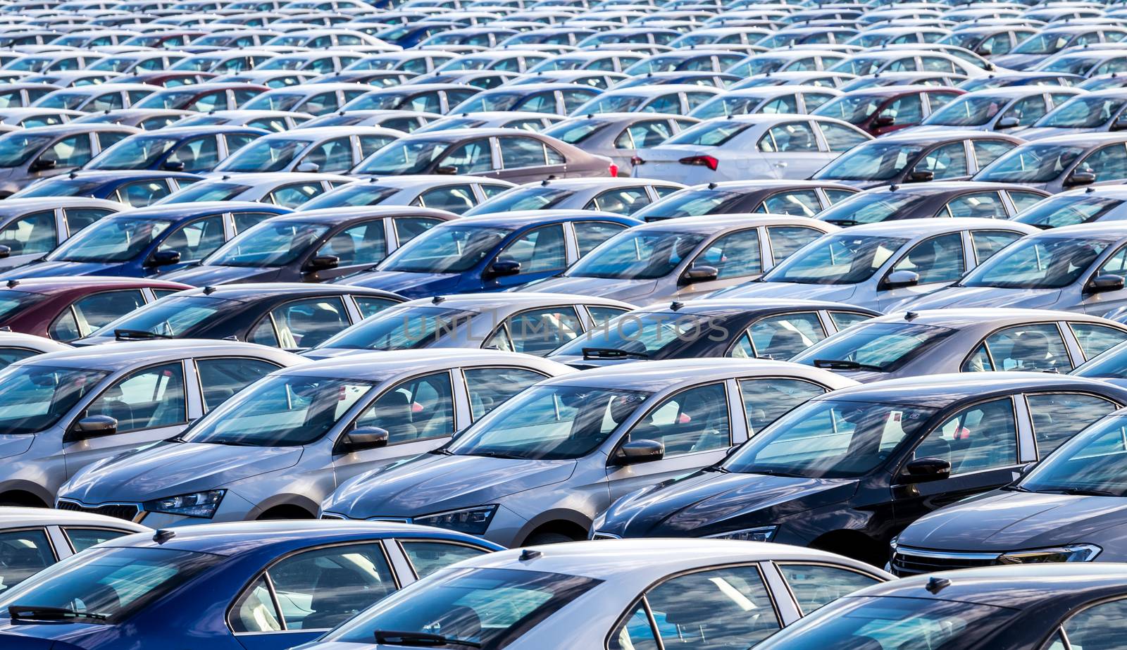 Rows of a new cars parked in a distribution center on a car factory on a sunny day. Top view to the parking in the open air.