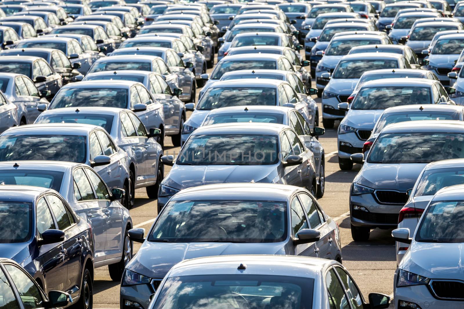 Rows of a new cars parked in a distribution center on a car factory on a sunny day. Top view to the parking in the open air.