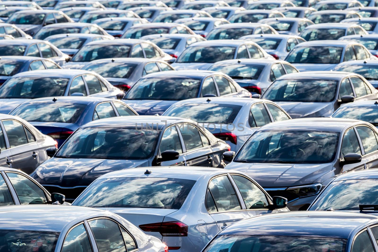 Rows of a new cars parked in a distribution center on a car factory on a sunny day. Top view to the parking in the open air.