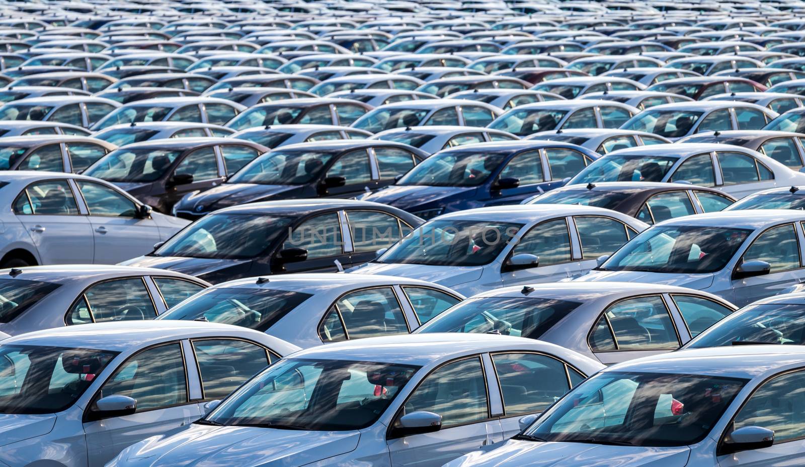 Rows of a new cars parked in a distribution center on a car factory on a sunny day. Top view to the parking in the open air.