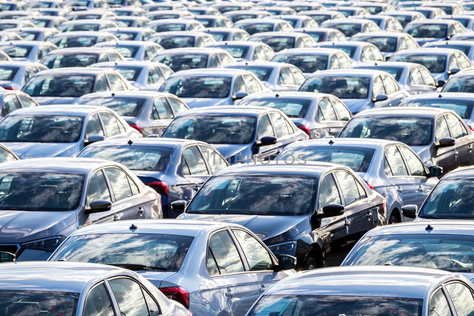 Rows of a new cars parked in a distribution center on a car factory on a sunny day. Parking in the open air.