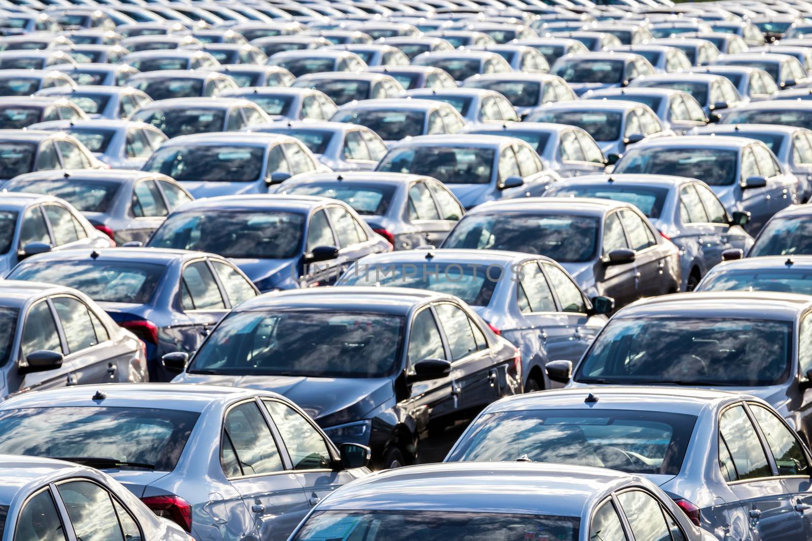 Rows of a new cars parked in a distribution center on a car factory on a sunny day. Top view to the parking in the open air.