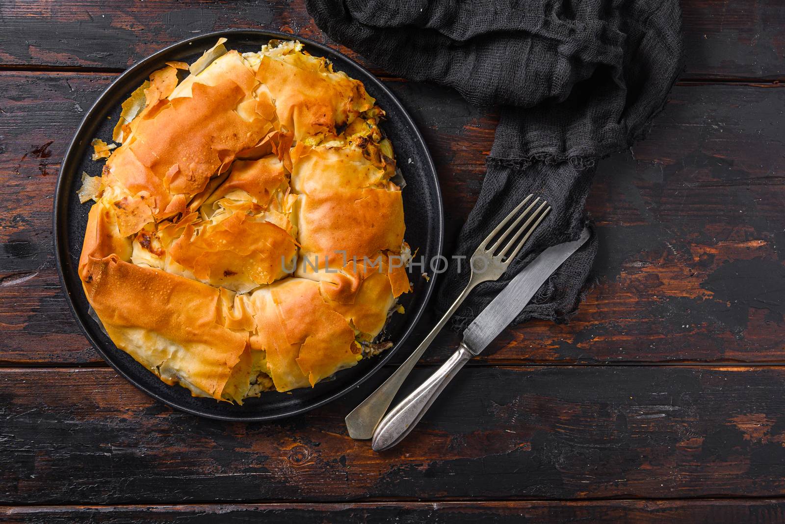 Homemade Greek spanakopita in on black plate filo spinach eggs feta top view on dark wooden background. Space for text