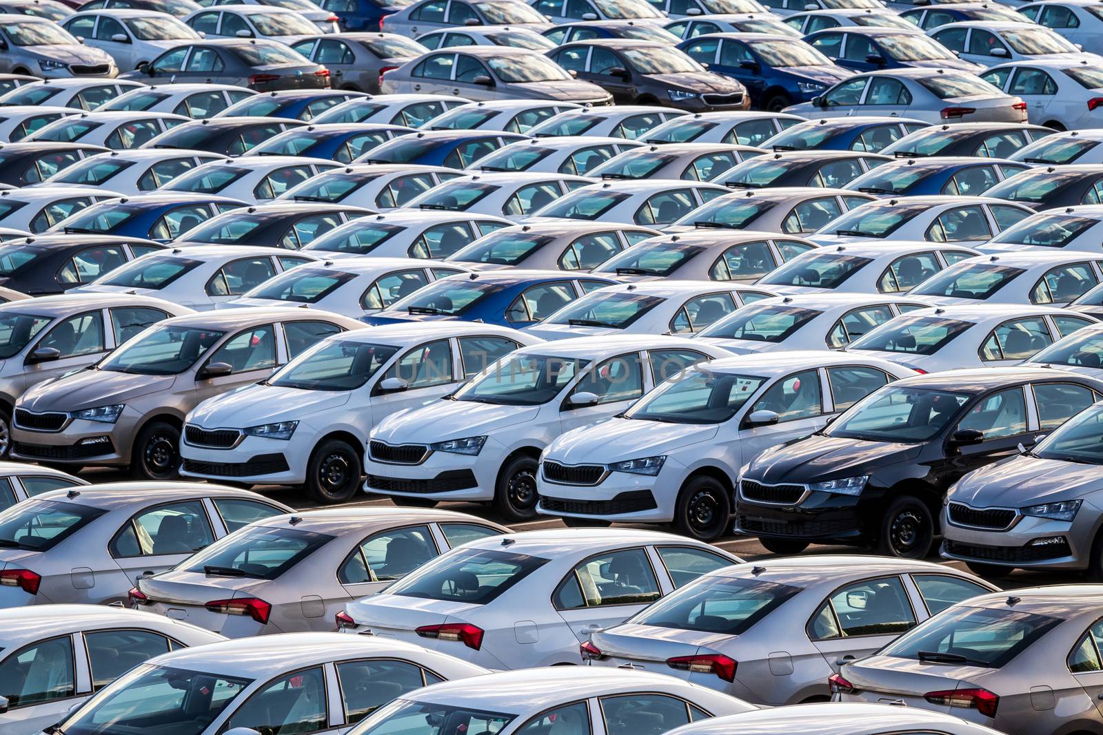 Rows of a new cars parked in a distribution center on a car factory on a sunny day. Top view to the parking in the open air.