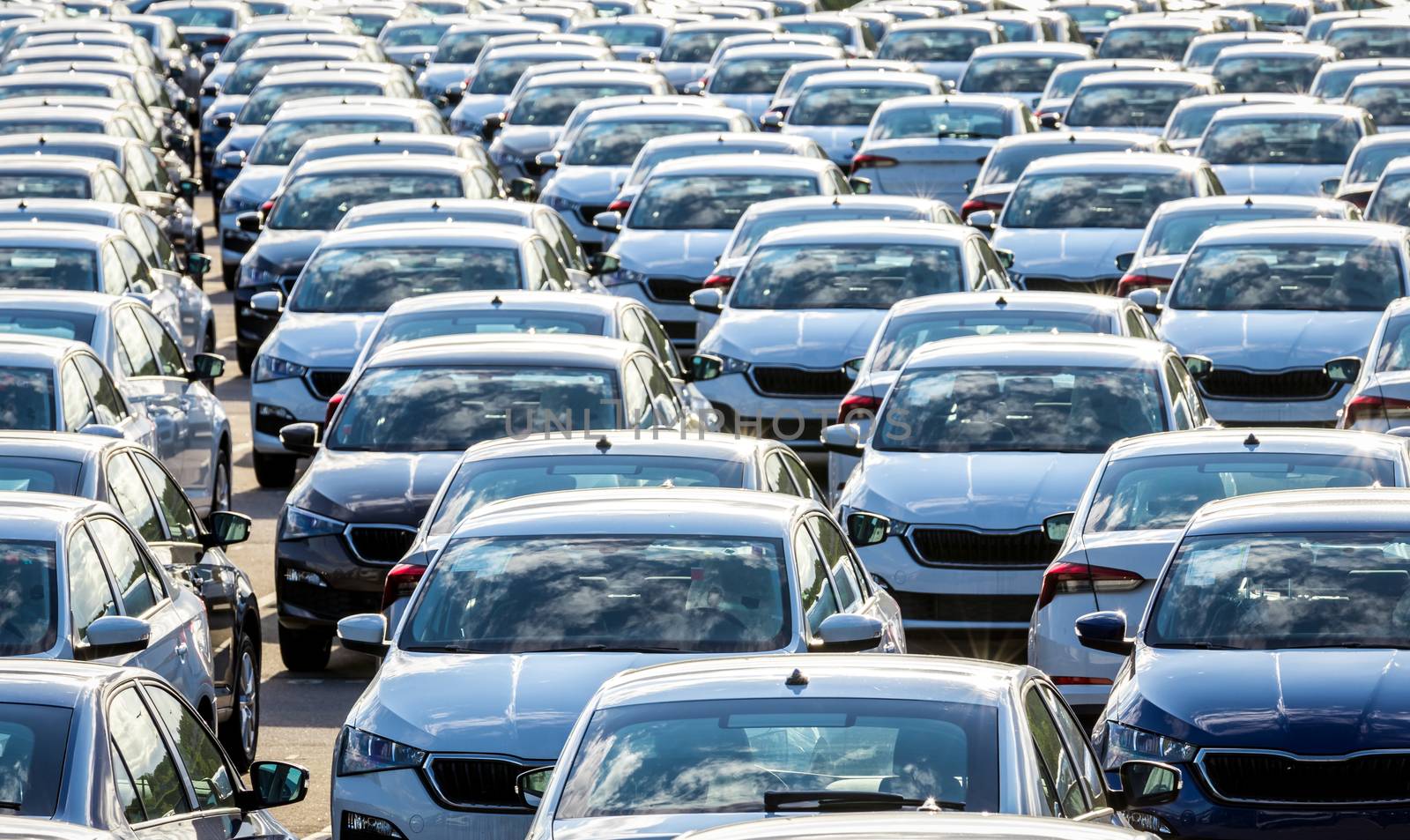 Rows of a new cars parked in a distribution center on a car factory on a sunny day. Top view to the parking in the open air.