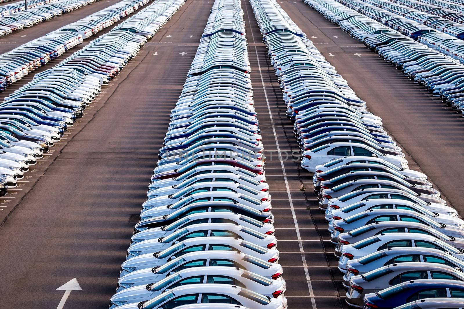 Rows of a new cars parked in a distribution center on a car factory on a sunny day. Top view to the parking in the open air.