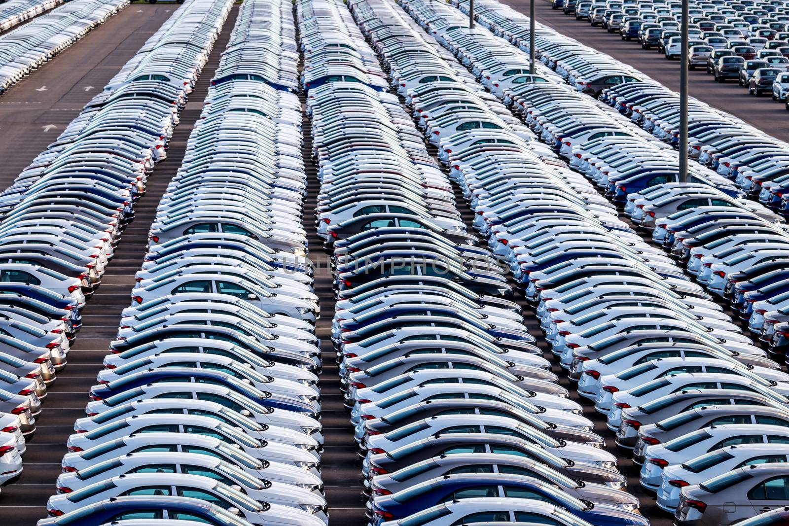 Rows of a new cars parked in a distribution center on a car factory on a sunny day. Parking in the open air.