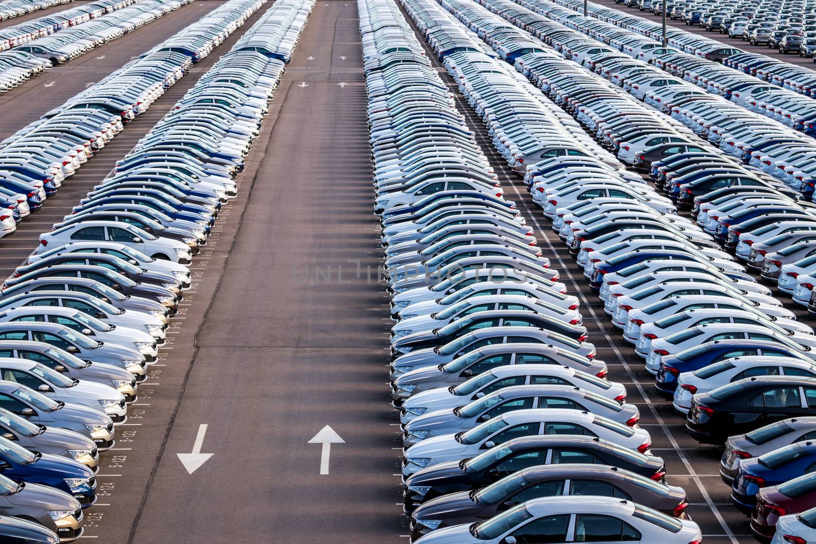 Rows of a new cars parked in a distribution center on a car factory on a sunny day. Parking in the open air.