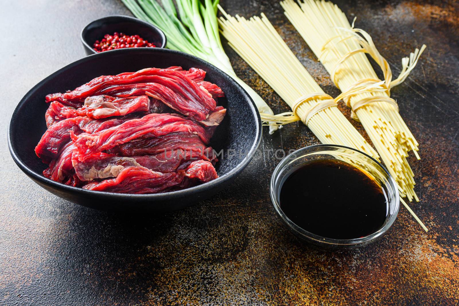 Raw ingredients for stir fry Chinese noodles with vegetables and beef in black bowl. On old rustic table. side view