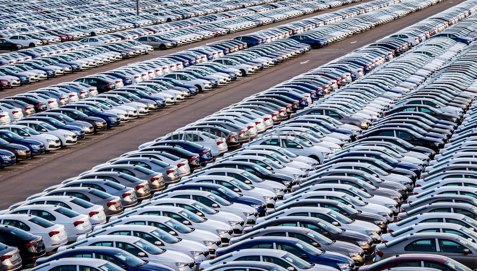 Rows of a new cars parked in a distribution center on a car factory on a sunny day. Top view to the parking in the open air.