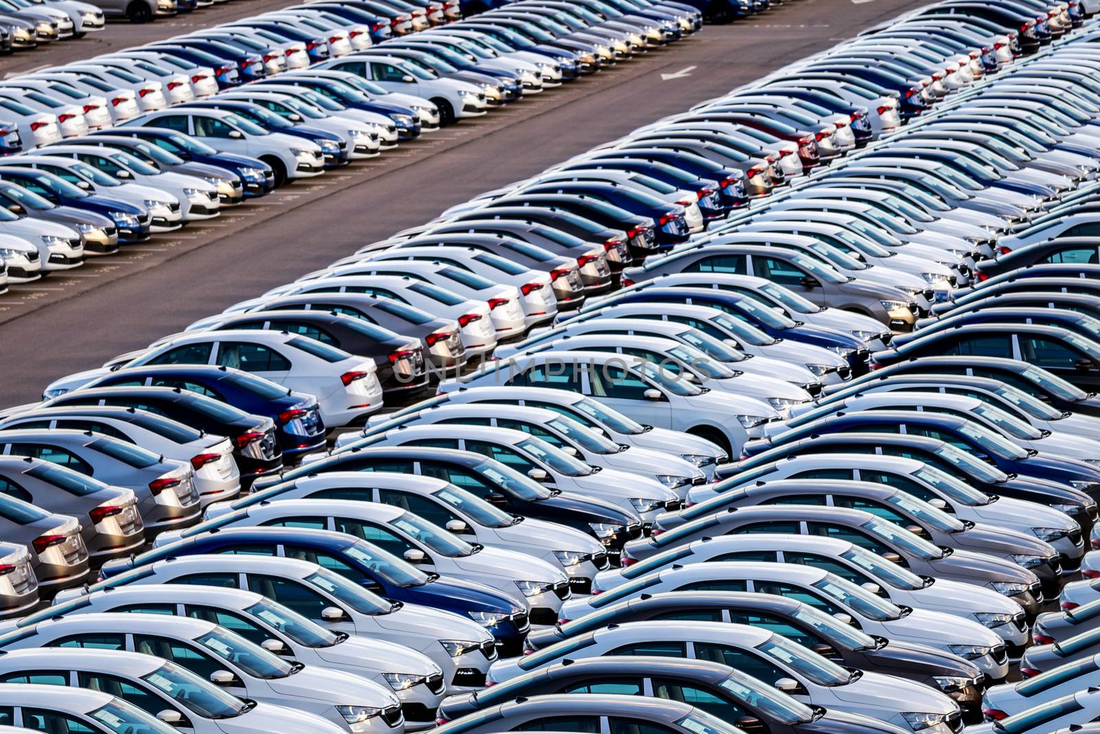 Rows of a new cars parked in a distribution center on a car factory on a sunny day. Top view to the parking in the open air.