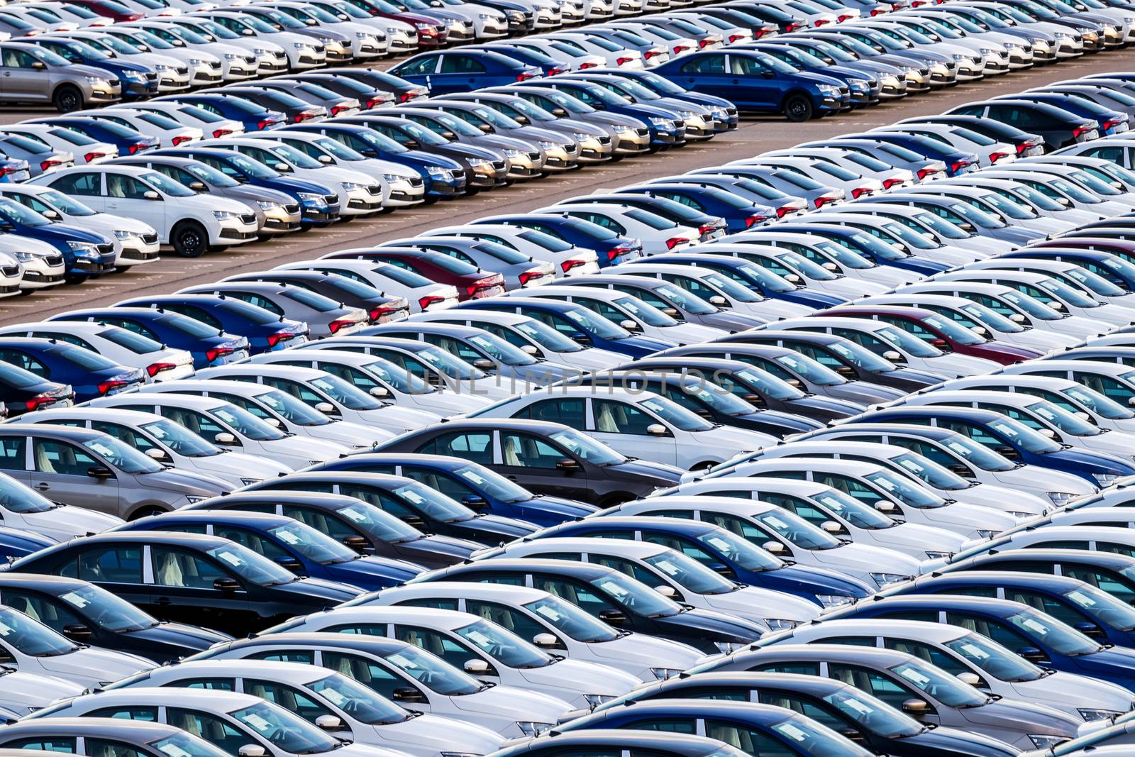 Rows of a new cars parked in a distribution center on a car factory on a sunny day. Top view to the parking in the open air.