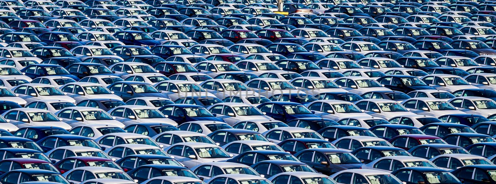 Rows of a new cars parked in a distribution center on a car factory on a sunny day. Parking in the open air.