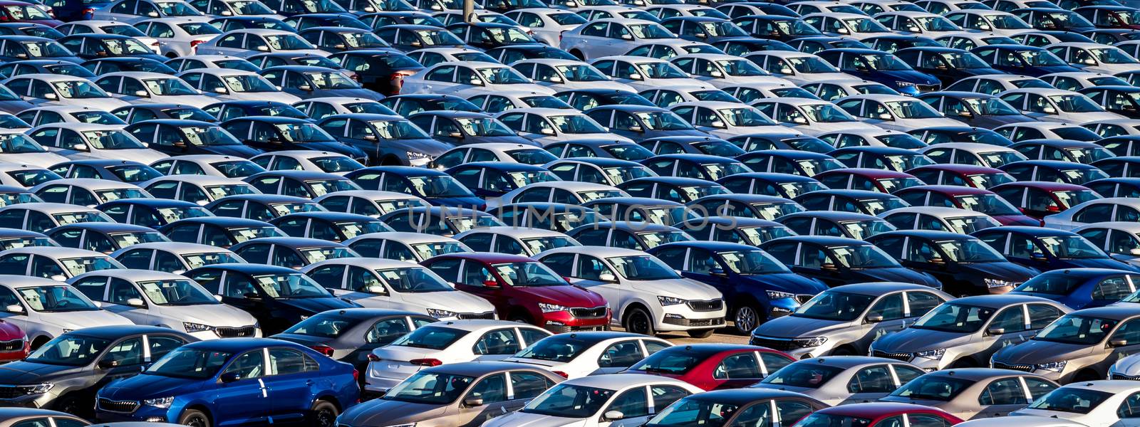 Rows of a new cars parked in a distribution center on a car factory on a sunny day. Top view to the parking in the open air.