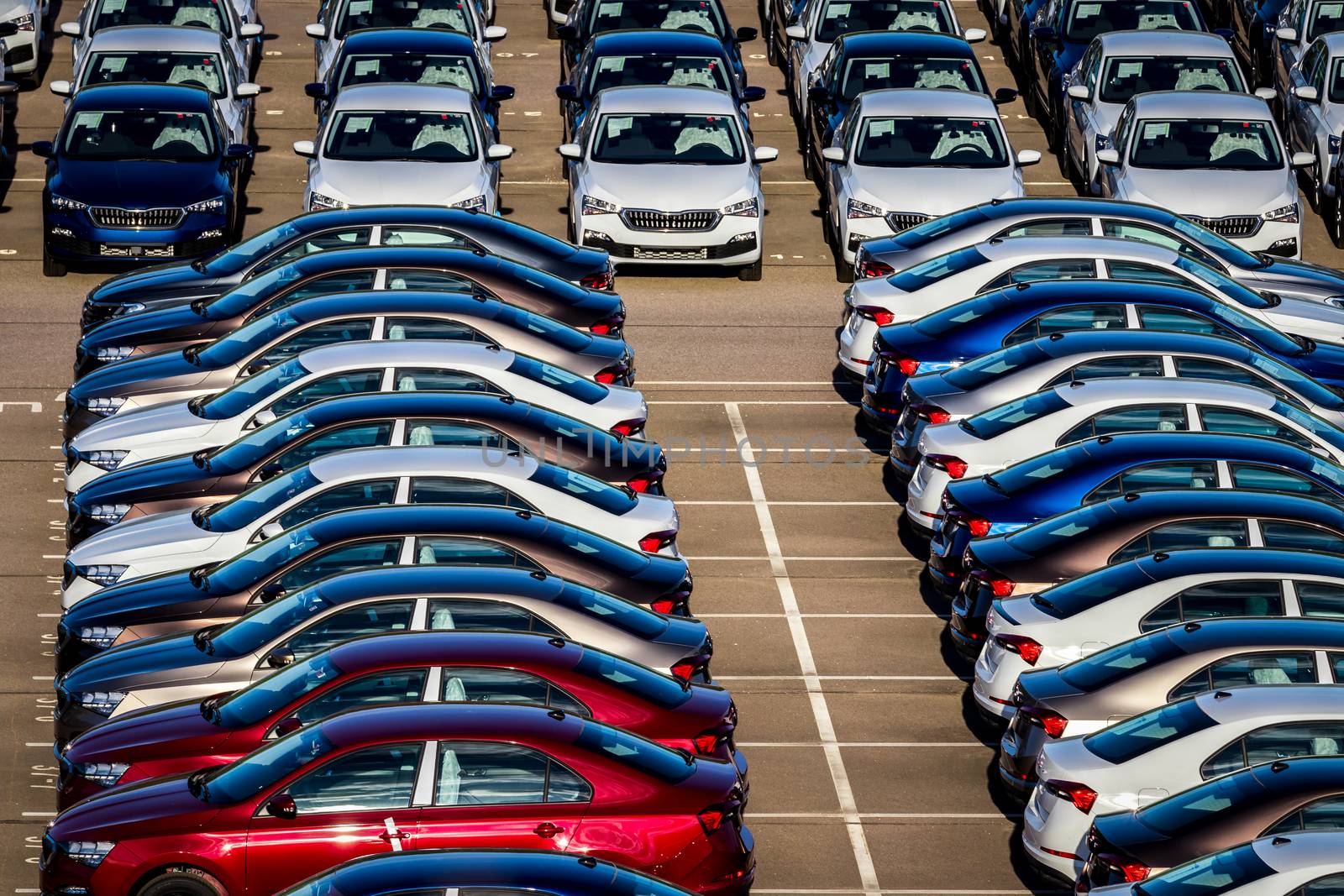 Rows of a new cars parked in a distribution center on a car factory on a sunny day. Top view to the parking in the open air.