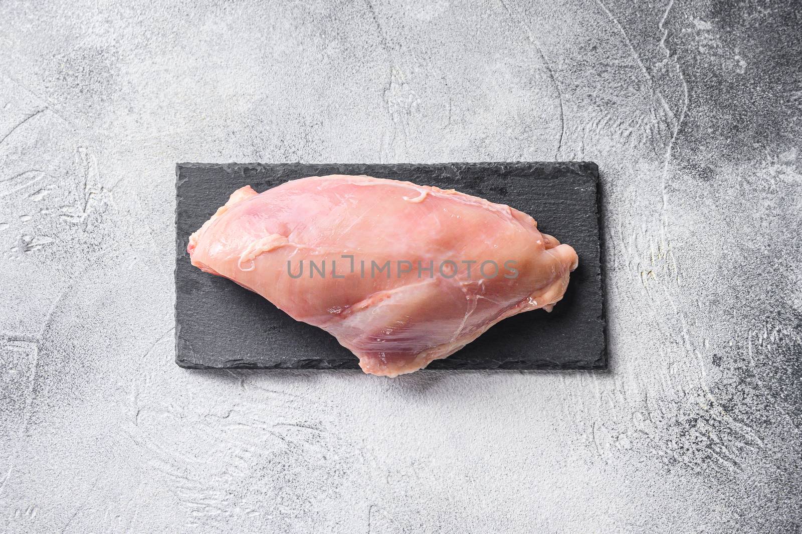 Raw chicken breast fillets on stone board over grey background.