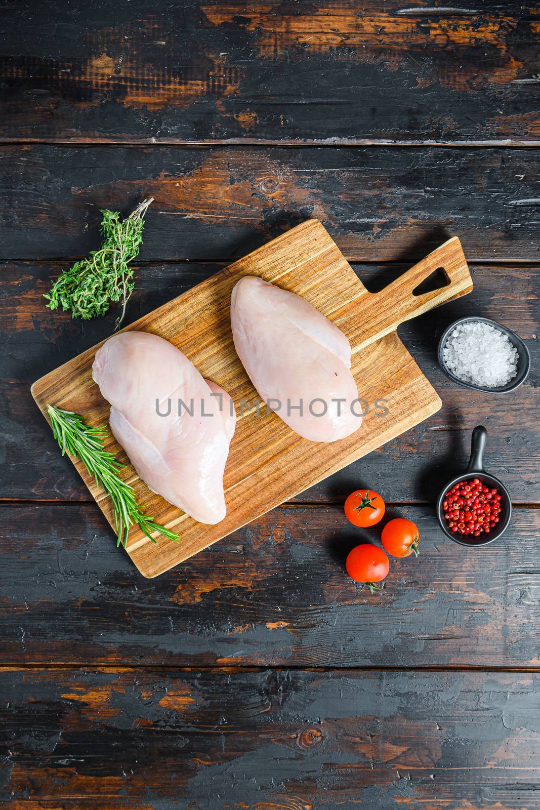 Raw chicken breast fillets and vegetable on chopping board overdark wooden background top view