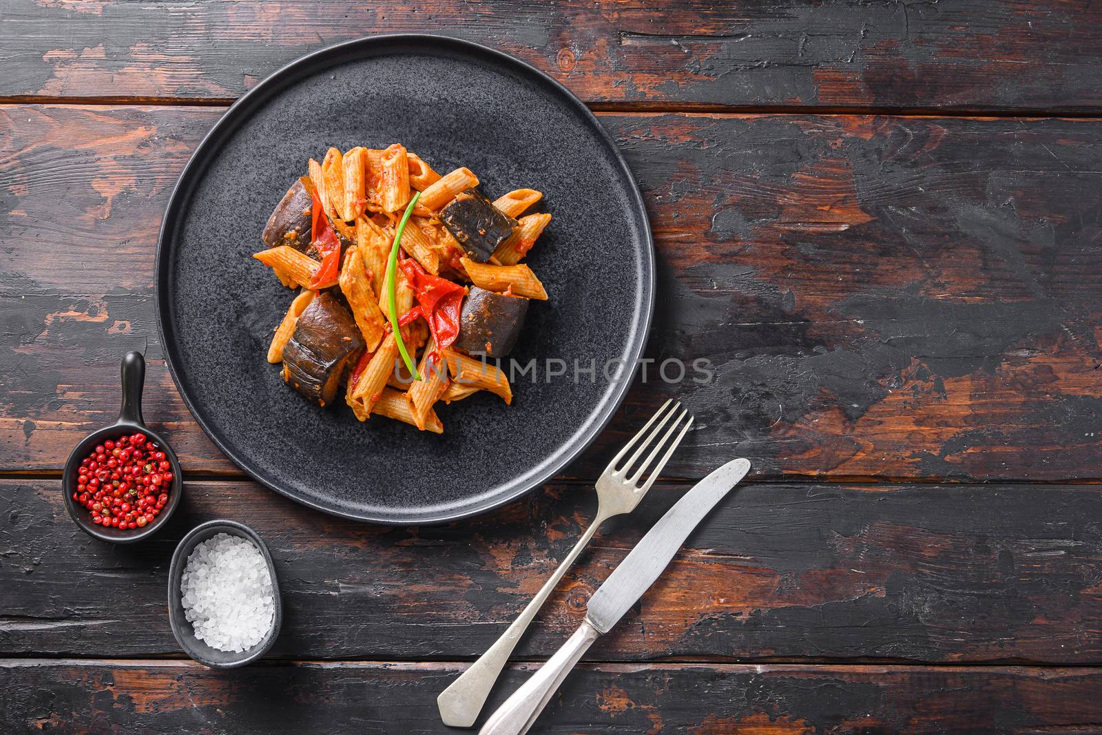 Aubergine penne eggplant pasta, pepper tomatoe sauce, on black plate over old dark wooden table served top view space for text