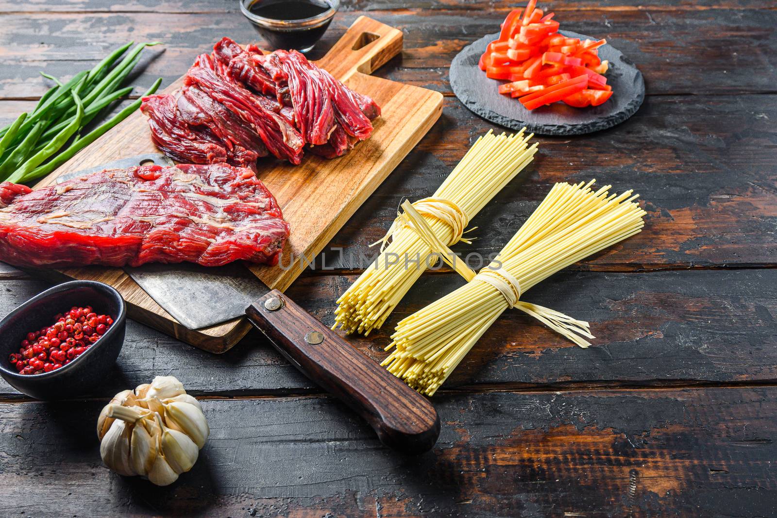 Chinese noodles with vegetables, . Machete steak and butcher cleaver over wooden background. Side view