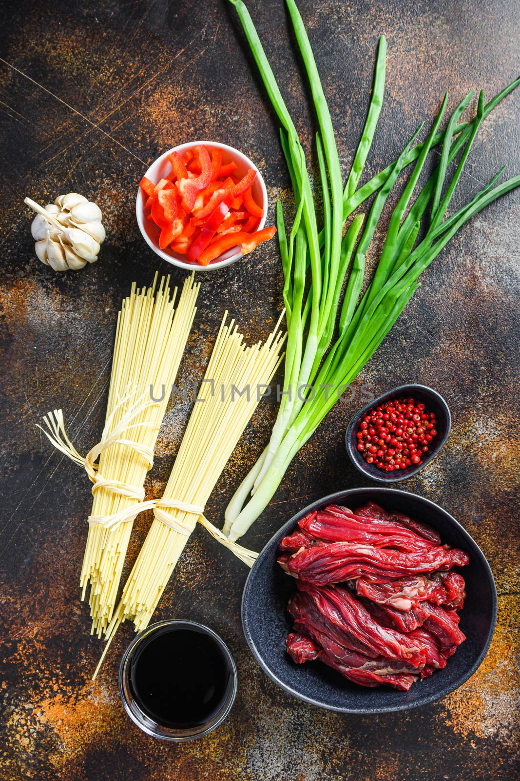 Raw ingredients for stir fry Chinese noodles with vegetables and beef in black bowl. On old rustic table. by Ilianesolenyi