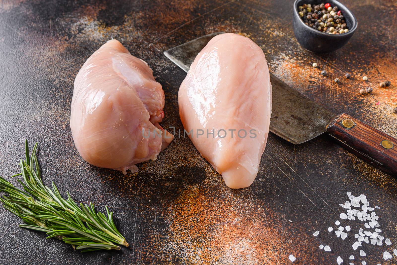 Farm chicken breast fillet, on meat cleaver spices and herbs onold rustic metall table side view.