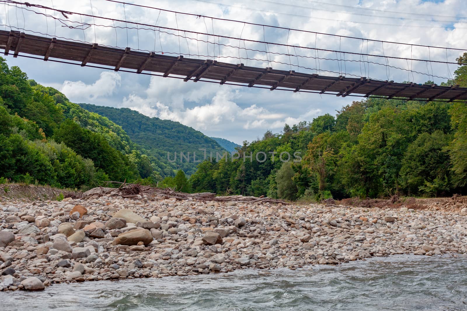 Suspension bridge over the mountain river at the summer cloudy day