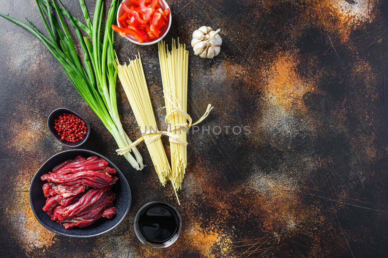 Raw ingredients for stir fry noodles with vegetables and beef in black bowl. On old rustic table. With space for text