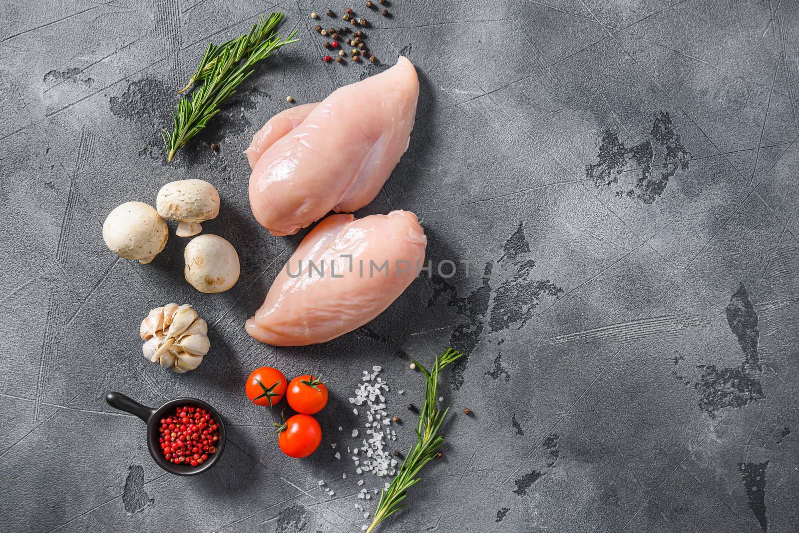 Organic chicken meat with garlic, pepper and rosemary on a grey concrete background top view space for text