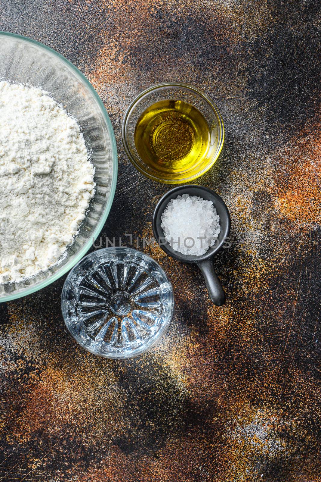Ingredients for the dough, flour oil water and salt on darkbackground vertical