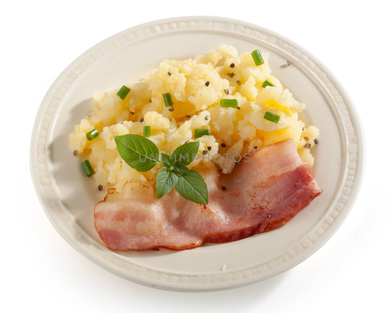 Mashed potatoes with fried bacon, basil and green onion on the white plate