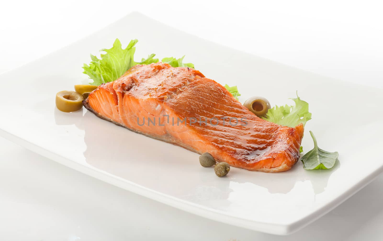 Baked fillet of trout with green lettuce and basil on the white plate