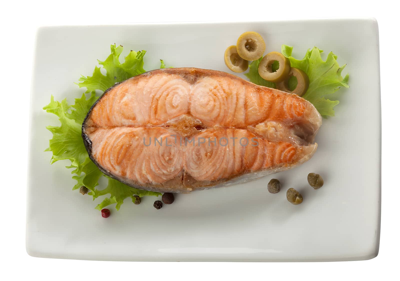 Baked steak of salmon with olives, capers and lettuce on the plate