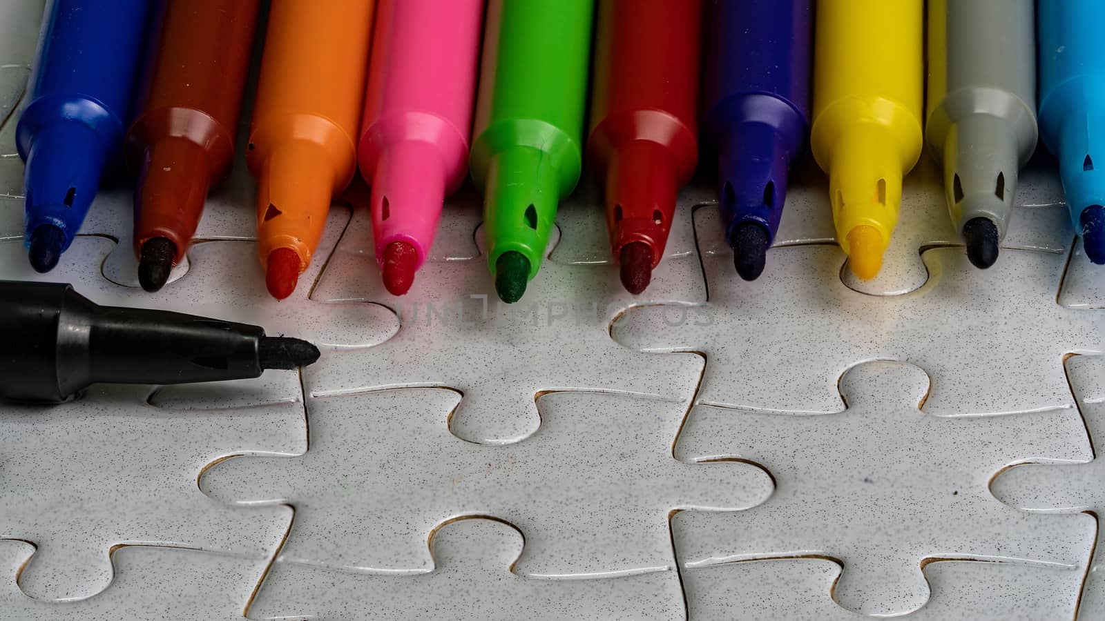 A multicolored pen on a white jigsaw background, color drawing device