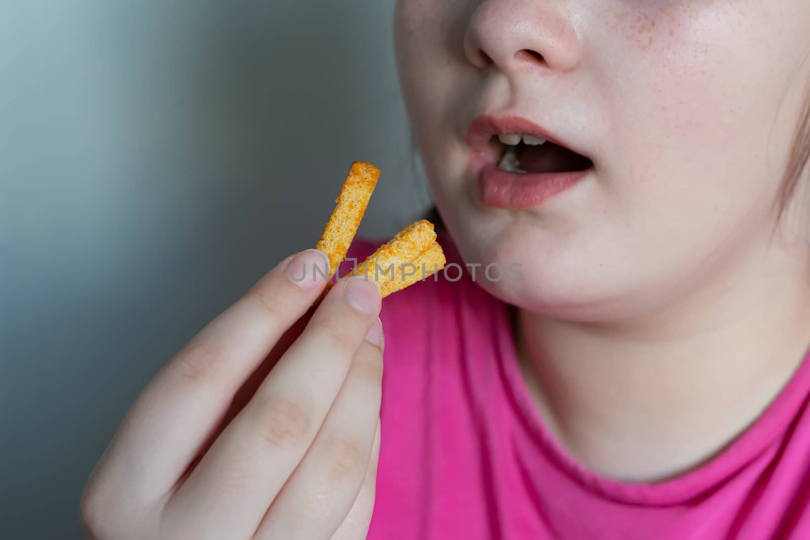 The girl puts in her mouth a few breadcrumbs. The girl eats crackers