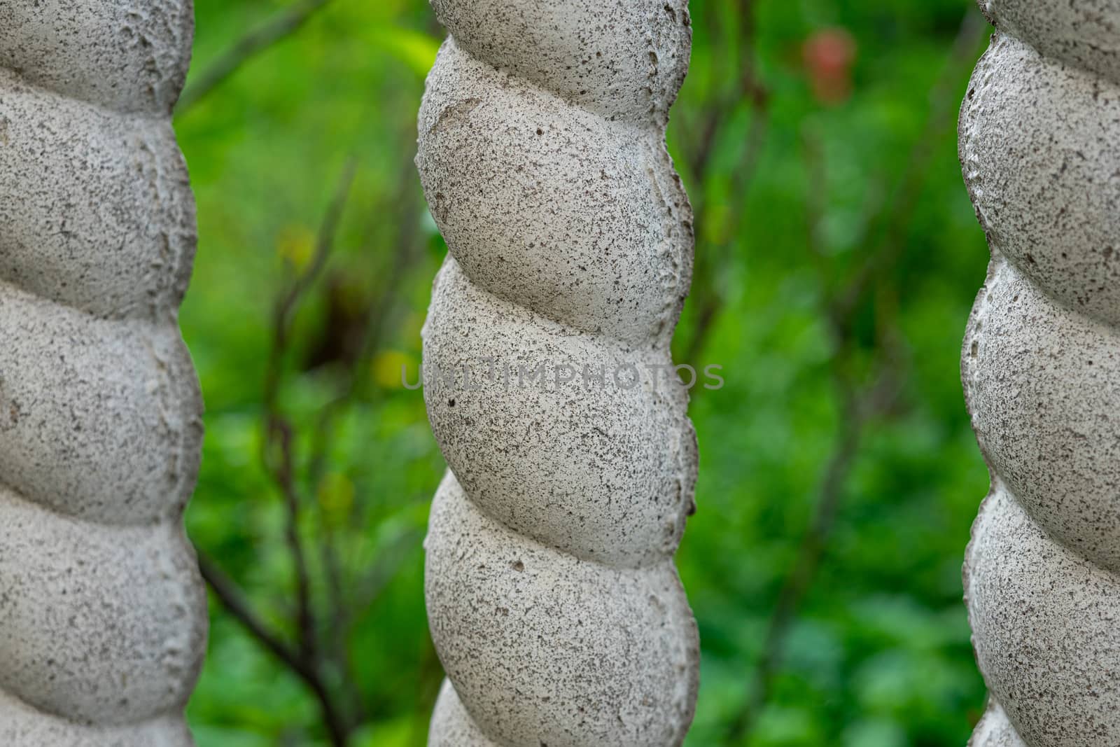 Part of a concrete fence in the form of a pigtail. Blurred green background