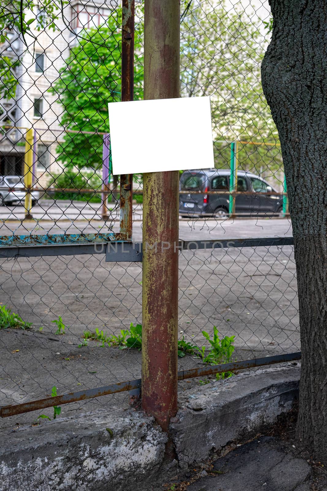 Basketball court fenced with a net. On the pillar hangs a sign for the inscription