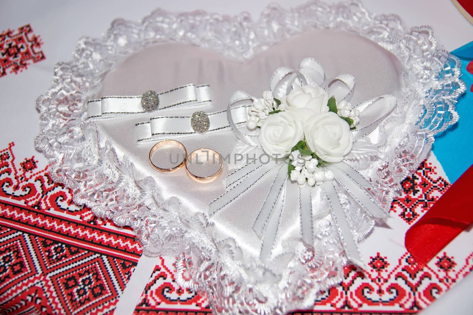 Wedding rings lie on a pillow in the form of a heart. Boutonniere and wedding rings. Ukrainian wedding embroidery close up.