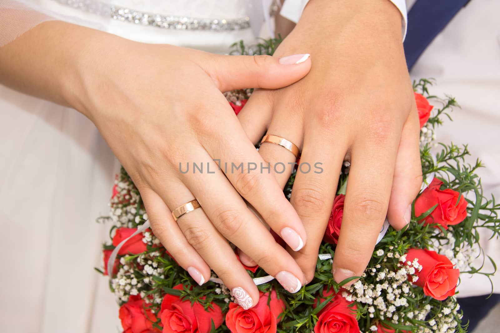 The bride and groom put their hands on a wedding bouquet of red roses. Together Forever