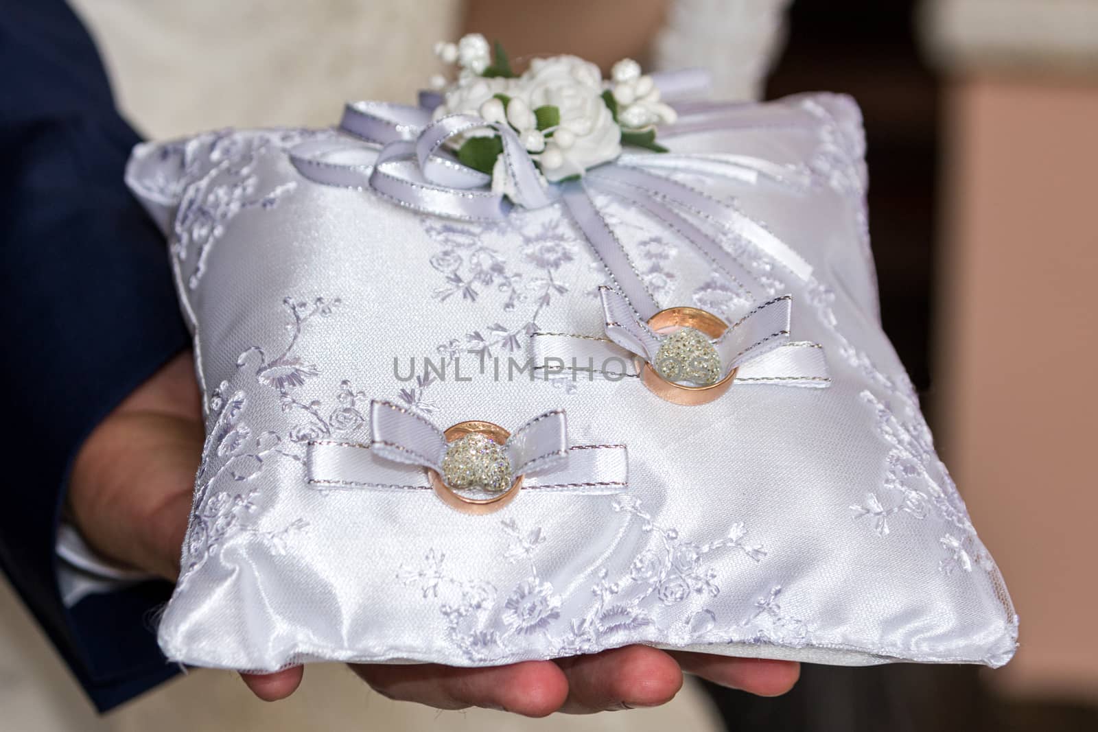 The groom holds a white pillow with wedding rings by Serhii_Voroshchuk