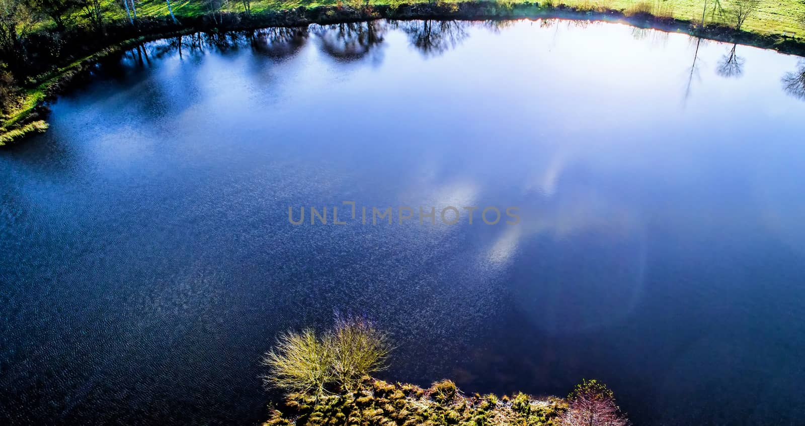 Pond in the back light with the reflections of the sun in the water, aerial photograph with the drone, intensified colours