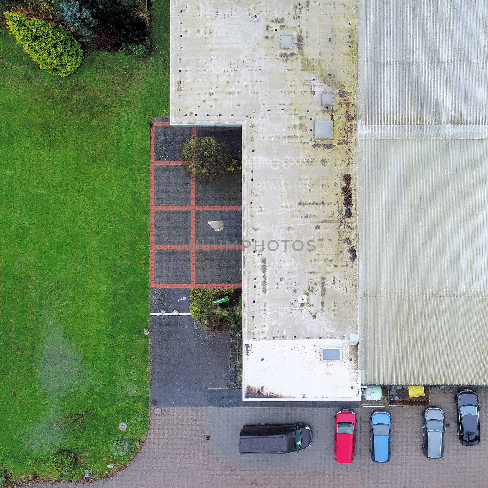 Cut vertical view from the air of an old, ugly tennis hall with parked cars in front of it, aerial view
