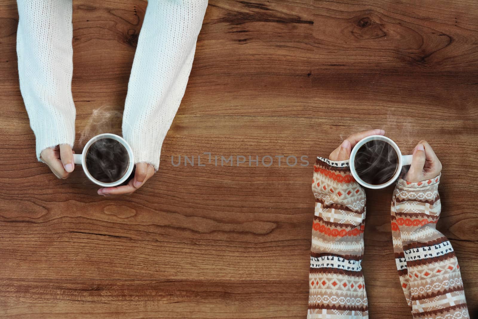 Female hands holding cups of coffee on rustic wooden table background by asiandelight